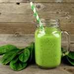 Healthy green smoothie with spinach in a jar mug against a wood background