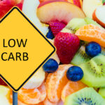 Yellow roadsign with message LOW CARB over background of healthy fresh fruits